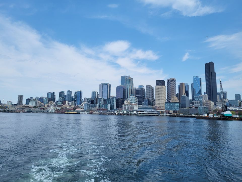 Panoramaaufnahme der Skyline von Seattle mit Wolkenkratzern und Wasser im Vordergrund unter blauem Himmel.